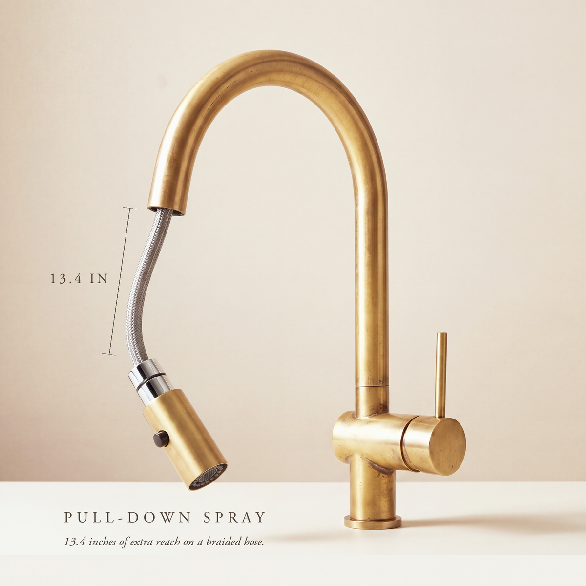 Unlacquered brass pull-down kitchen faucet with the spray head pulled out on its braided hose